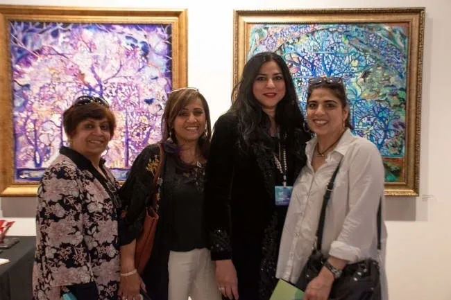 Four women standing in front of two paintings.