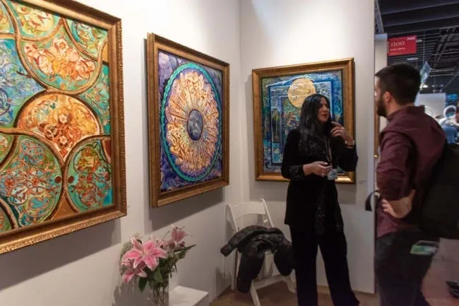 A woman standing in front of three paintings.